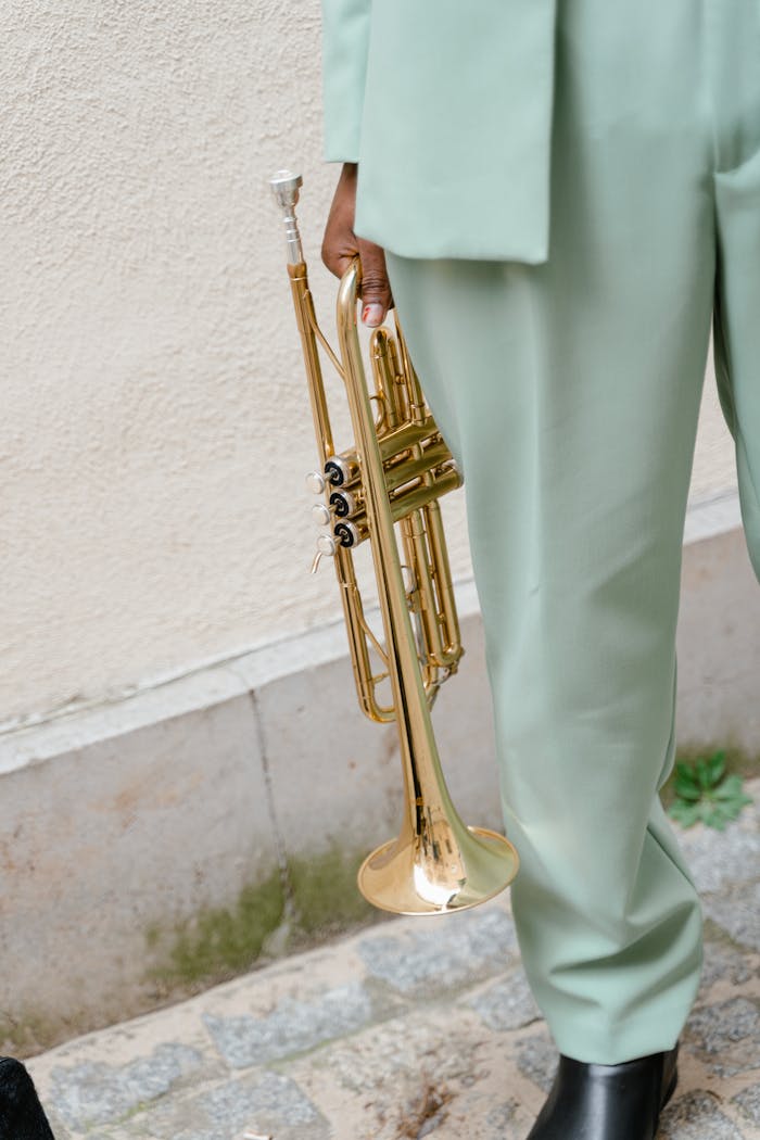 A person in pastel suit holding a brass trumpet on a sidewalk.